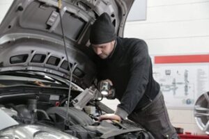 man in a black jacket and black knit cap inspecting car engine & motor oil